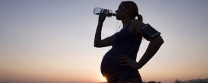 silhouette of pregnant athlete drinking water in front of the sunrise